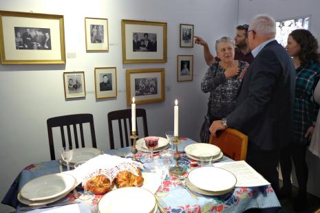 Am Shabbat-Tisch ist Pnina Drach (Israel) in ein Gespräch vertieft mit Peter Bleser (MdB). Unter den Familienfotos im Hintergrund befindet sich auch ihre Großmutter Alma Mayer.